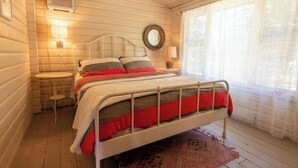 Um quarto aconchegante com cama, mesa de cabeceira, abajur e uma janela com cortinas.