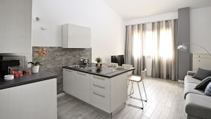 A modern kitchen with a central island, a dining area with a bar stool, and a living space with a sofa. - Boutique Apartment "Divided Two" in Florence (Firenze)