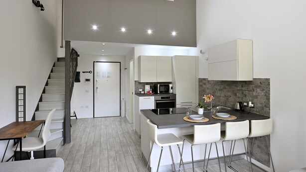 A modern kitchen with a central island, white bar stools, and a staircase leading to an upper level. - Boutique Apartment "Divided Two" in Florence (Firenze)
