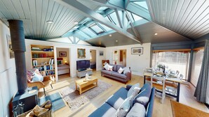A spacious living room with a high ceiling, a fireplace, a television, a sofa, a dining table, and a bookshelf.