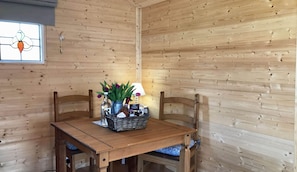 A wooden interior with a table set for two, featuring a vase with flowers and a basket of items.