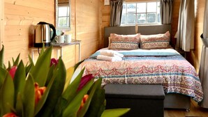 A wooden cabin room with a bed, a table with a kettle, and a window with curtains. - Arniss - sleeps 20 guests  in 9 bedrooms (Fordingbridge)