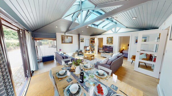 A spacious living area with a high ceiling, a dining table set for four, a sofa, and a television.