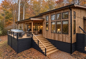 A wooden cabin with a hot tub, outdoor seating, and a staircase leading to the entrance.