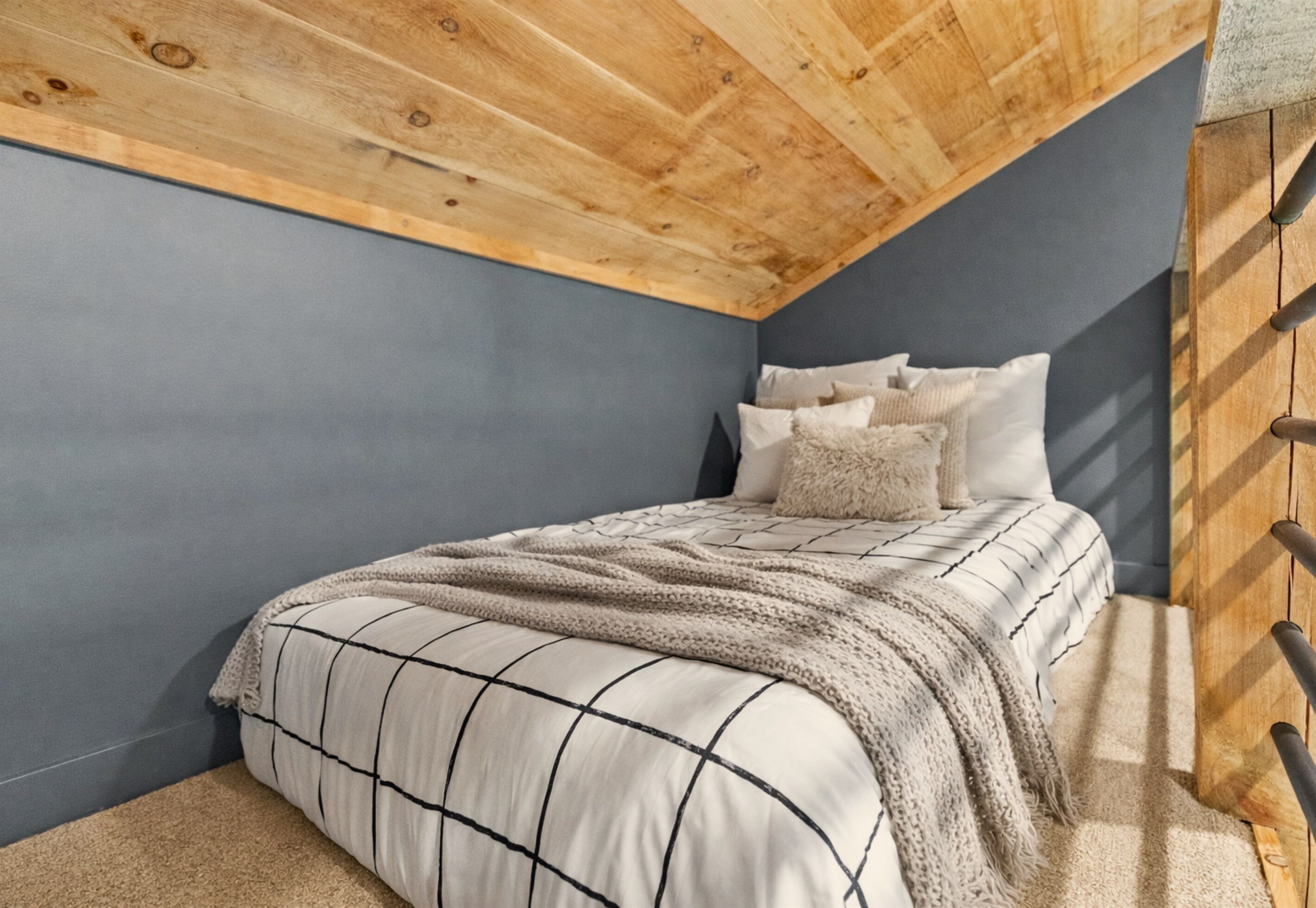 A bedroom with a sloped ceiling, a bed with a patterned bedspread, and a wooden wall.