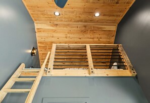 Une pièce avec un plafond en bois, une échelle et une rambarde en métal.