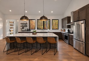 A modern kitchen with a large island, stainless steel appliances, and pendant lighting.