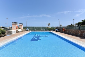 Una piscina cristallina con un galleggiante, sedie a sdraio e un muro in pietra.