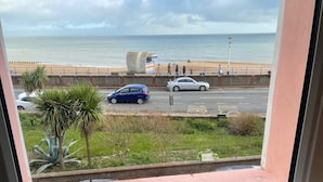 Vista di una spiaggia con una scultura in cemento, una strada con auto e una palma.