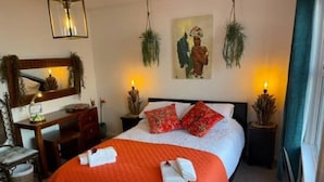 Una camera da letto con un letto, comodini, una scrivania, una sedia e una pianta pensile.