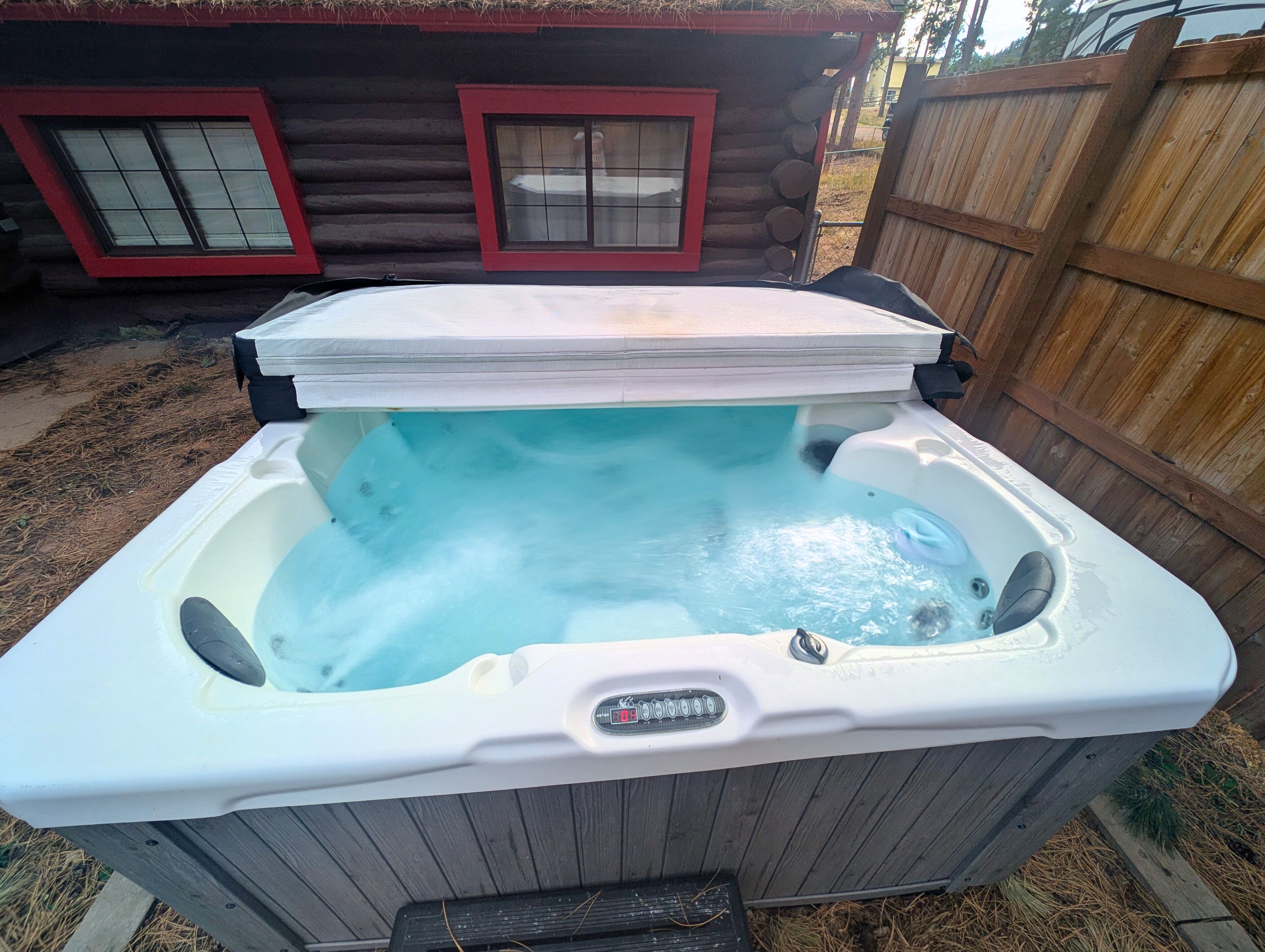A hot tub with a digital timer, surrounded by a wooden deck and a log cabin in the background.
