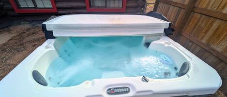 A hot tub with a digital timer, surrounded by a wooden deck and a log cabin in the background.