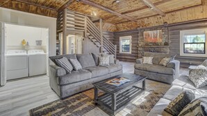 Et interiør af en hytte med en opholdsstue, der indeholder to grå sofaer, et sofabord og en trappe til et loft.