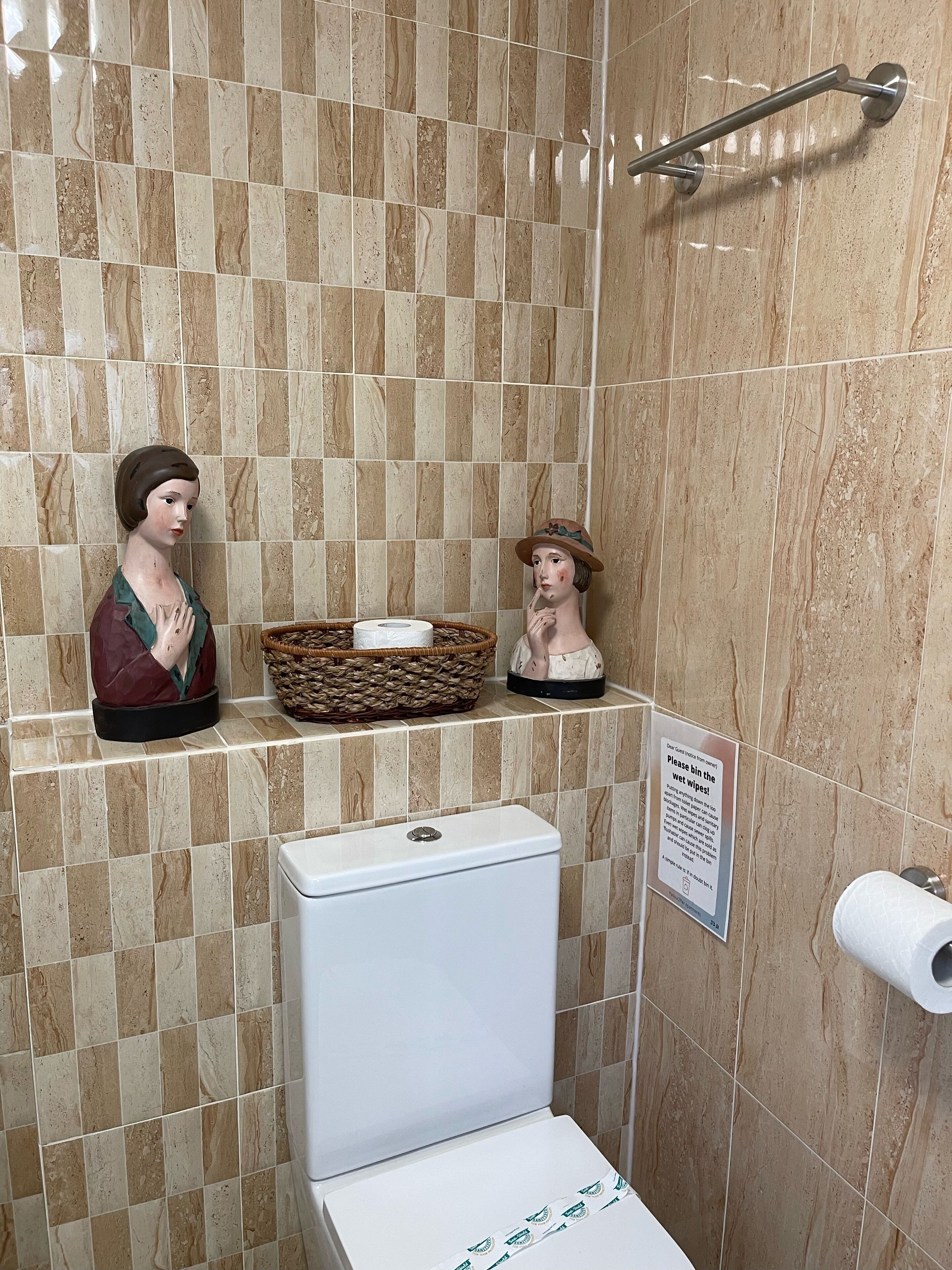 A bathroom with a toilet, a hand dryer, and a sign instructing to bin wet wipes.