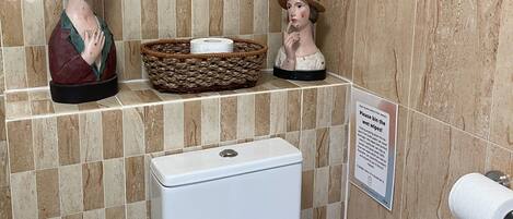 A bathroom with a toilet, a hand dryer, and a sign instructing to bin wet wipes.