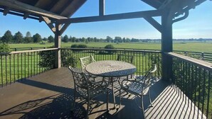 A covered outdoor area with a table and chairs, overlooking a green field. - The Cabin at Denali Stud (Paris)
