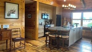 A wooden cabin interior with a kitchen, dining area, and a large window. - The Cabin at Denali Stud (Paris)