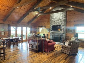 A spacious room with a stone fireplace, wooden ceiling beams, and a television mounted on the wall. - The Cabin at Denali Stud (Paris)