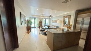 Una cocina moderna con una isla central, un comedor con sofá y un gran ventanal que proporciona luz natural.