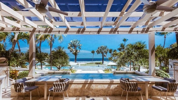 Zona junto a la piscina con vistas al océano, mobiliario exterior y una pérgola.
