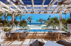 A poolside area with a view of the ocean, outdoor seating, and a pergola structure.