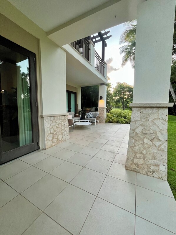 A covered outdoor patio with a dining area, stone columns, and a view of the surrounding greenery.