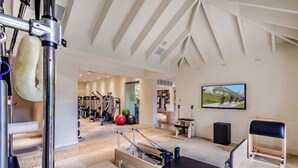 Un gimnasio con equipamiento de ejercicio, un reformador de Pilates y una televisión mostrando una competición de ciclismo.