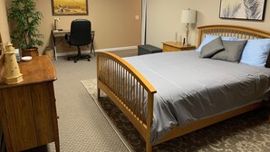 A hotel room with a wooden bed, a desk with a chair, a lamp, a potted plant, and a painting on the wall. - BlueRidgeVista.  4 miles to Tryon Equestrian Ctr. (Rutherfordton)