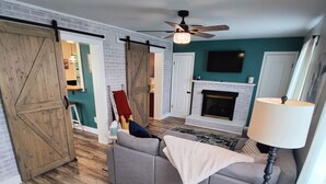 Un salon spacieux avec un canapé gris, un plancher en bois, une cheminée et un ventilateur de plafond.