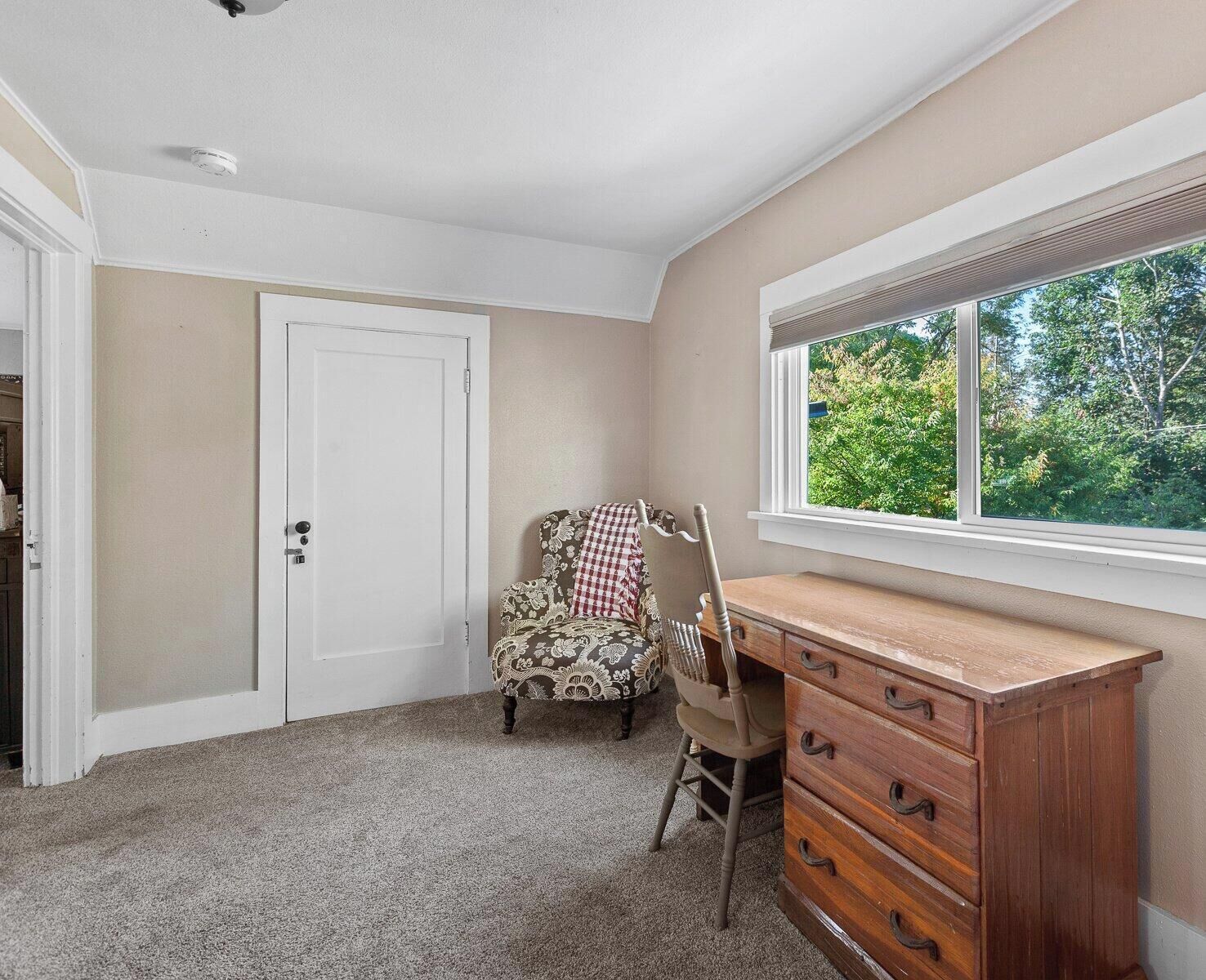 Une pièce avec un bureau en bois, une chaise, une porte et une fenêtre donnant sur des arbres.