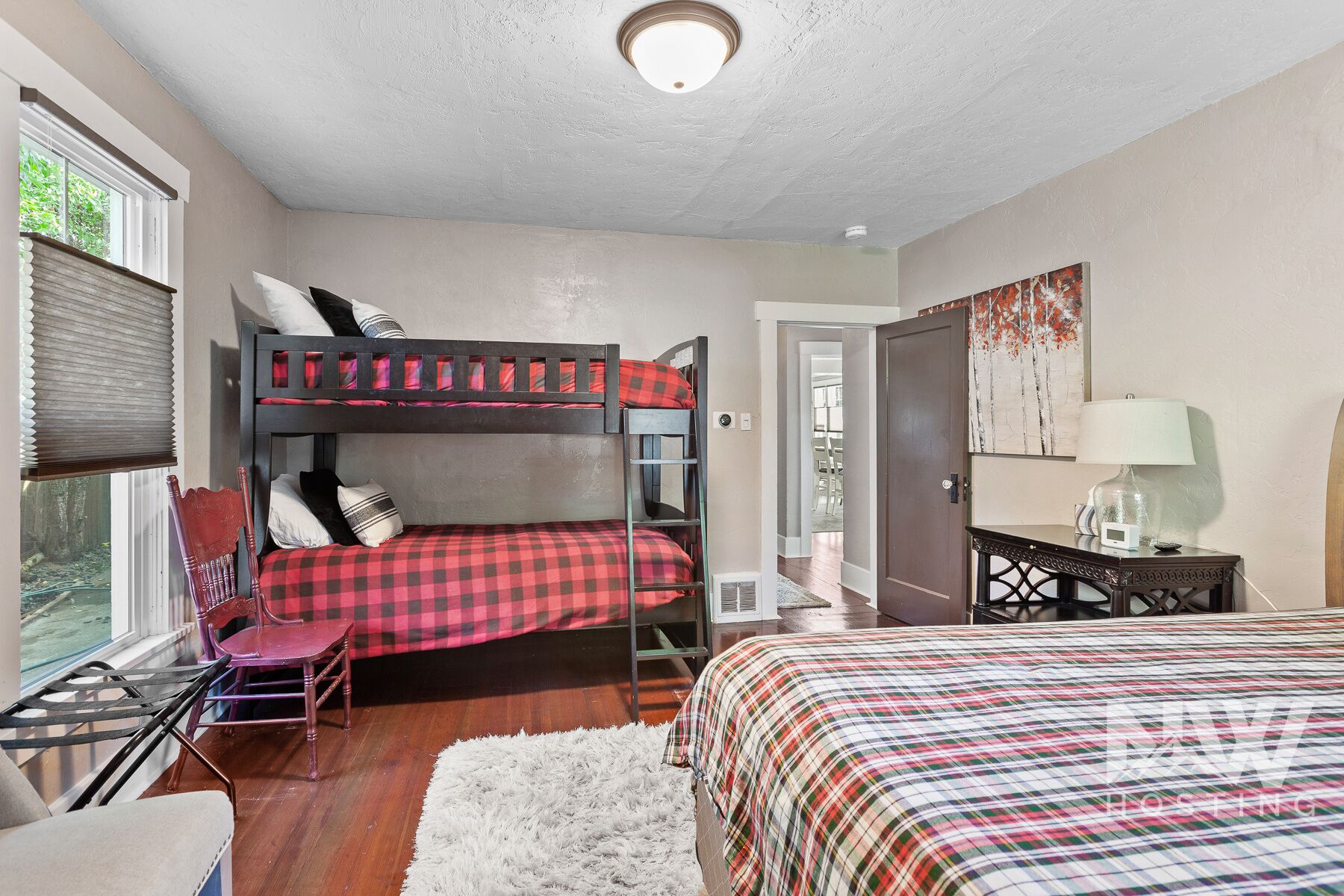 Une chambre avec des lits superposés, un bureau, une chaise et un lit recouvert d’une couverture à carreaux.