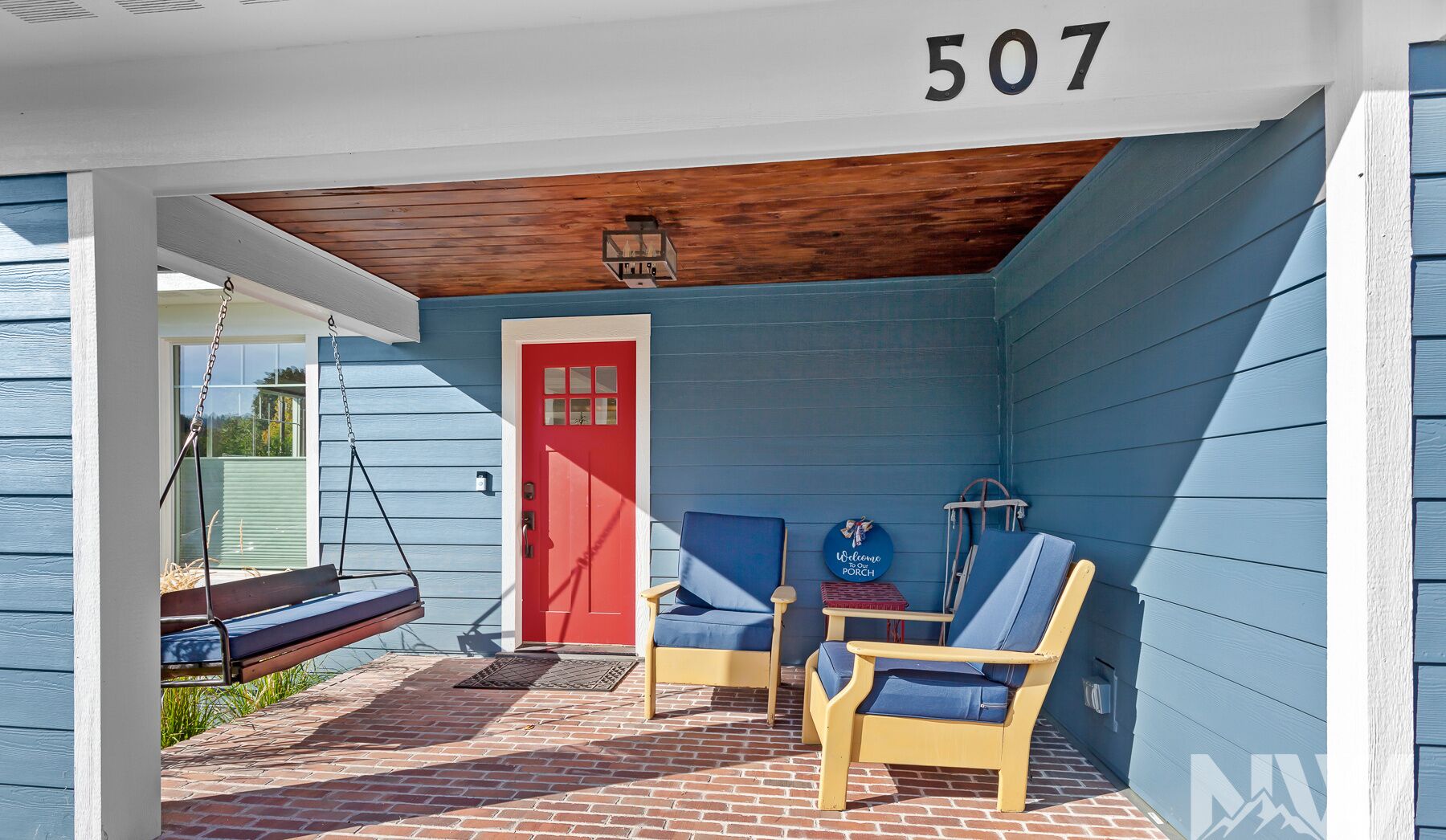 A porch with a swing, a red door, and two blue chairs.