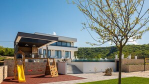 Une maison moderne avec un patio, un toboggan et un arbre.