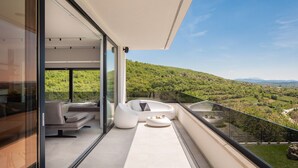 Un balcon moderne doté d’une balustrade en verre, d’un canapé, d’un fauteuil et d’une petite table.