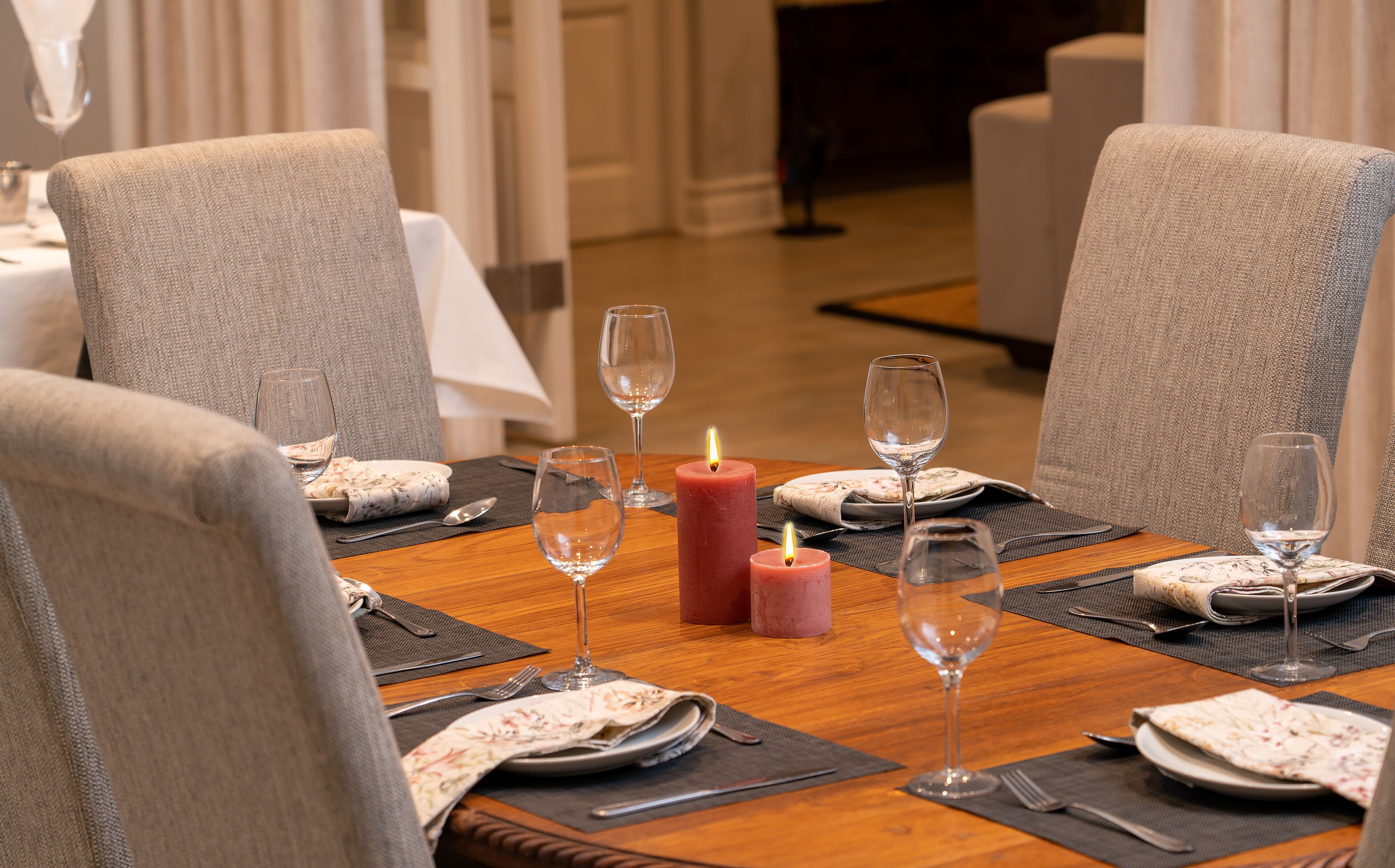 A dining table set for four with a candle centerpiece, wine glasses, and a floral tablecloth.