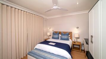 Una habitación de hotel con una cama grande, dos mesitas de noche, un ventilador de techo y un escritorio con una silla.