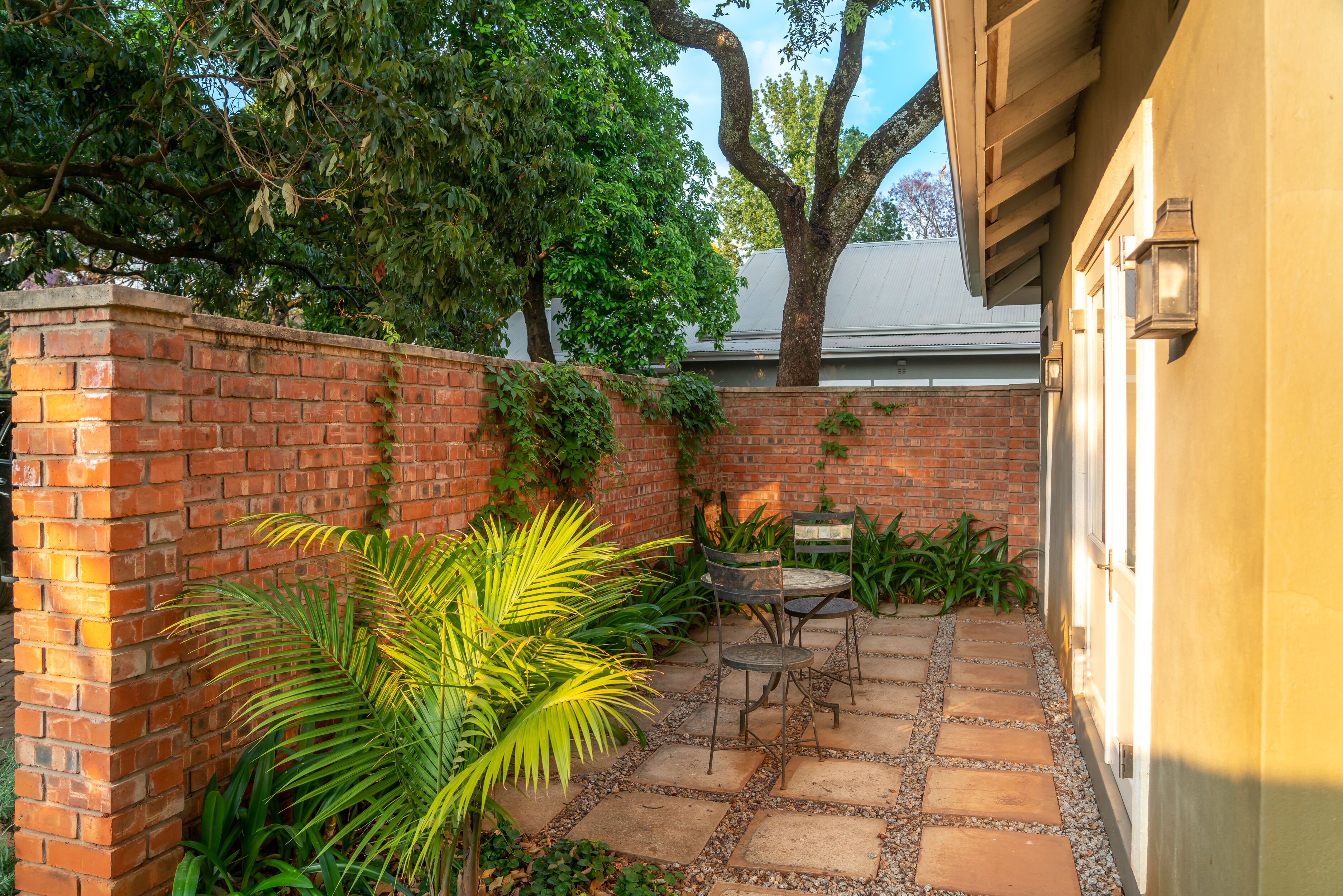 A patio with a brick wall, a palm tree, and a table with chairs.