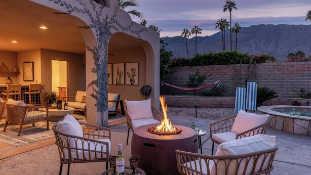 An outdoor patio with wicker furniture, a central fire pit, and a view of mountains. - Casa Del Lobo - Private Spanish Oasis Getaway (Palm Springs)
