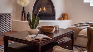 A cozy living room with a fireplace, a coffee table with a book, a vase with a plant, and a patterned wall. - Casa Del Lobo - Private Spanish Oasis Getaway (Palm Springs)