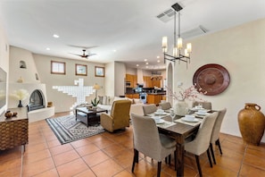 Amplia sala de estar con mesa de comedor para cuatro personas, chimenea y cocina al fondo.