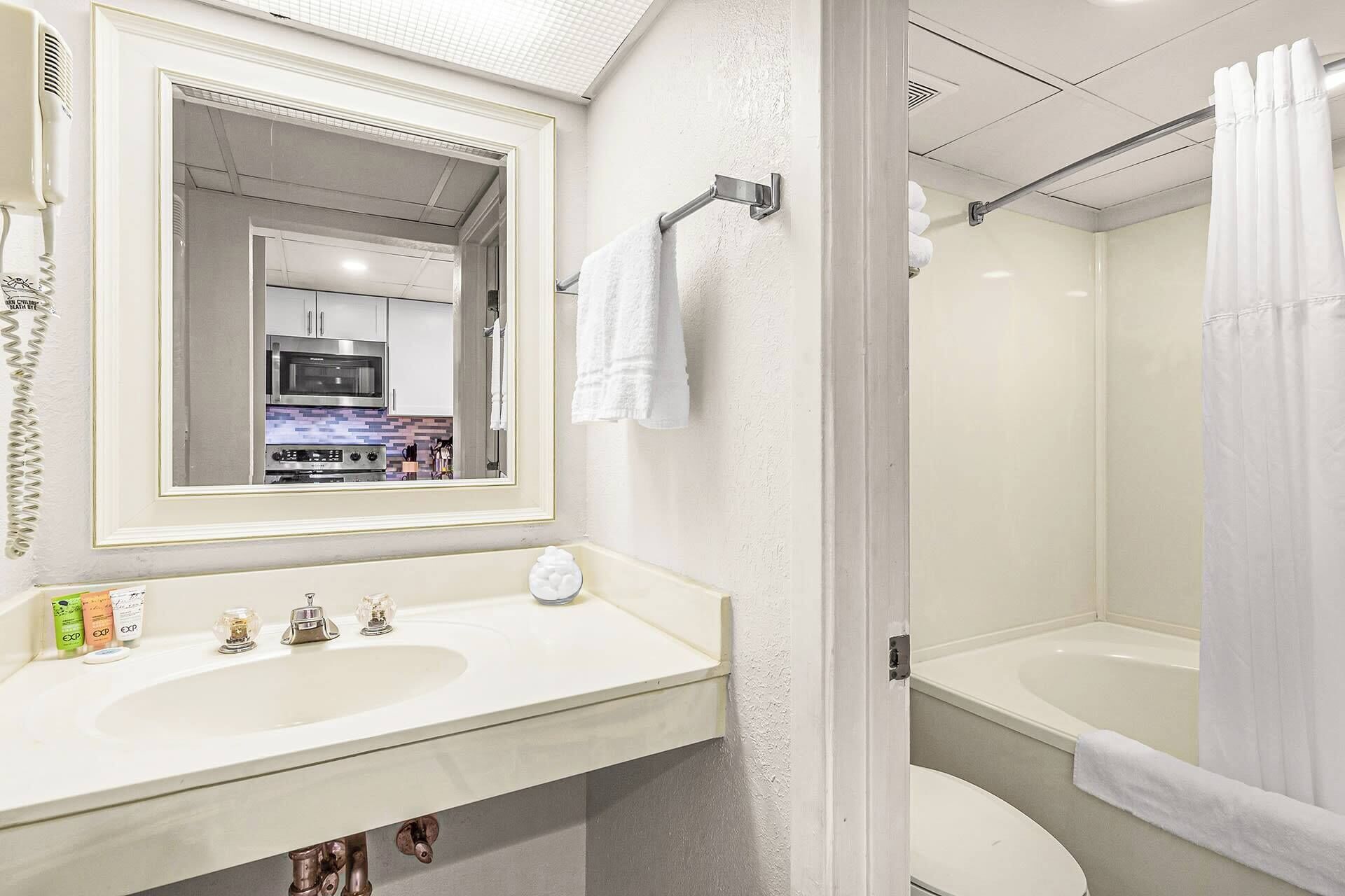 A bathroom with a white sink, mirror, and bathtub. There is a towel hanging on the wall and a shower curtain.