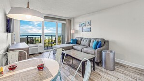 Un salon moderne comprenant un canapé, une table basse et un coin repas. Il y a un balcon avec vue sur l’océan.