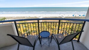 Un balcón con vista a la playa, dos sillas y una mesita.
