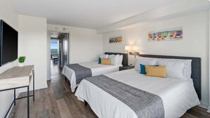 Habitación de hotel con dos camas, un escritorio, un televisor y vista al mar.