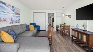Una sala de estar moderna con un sofá seccional gris, piso de madera y un comedor con mesa y sillas.