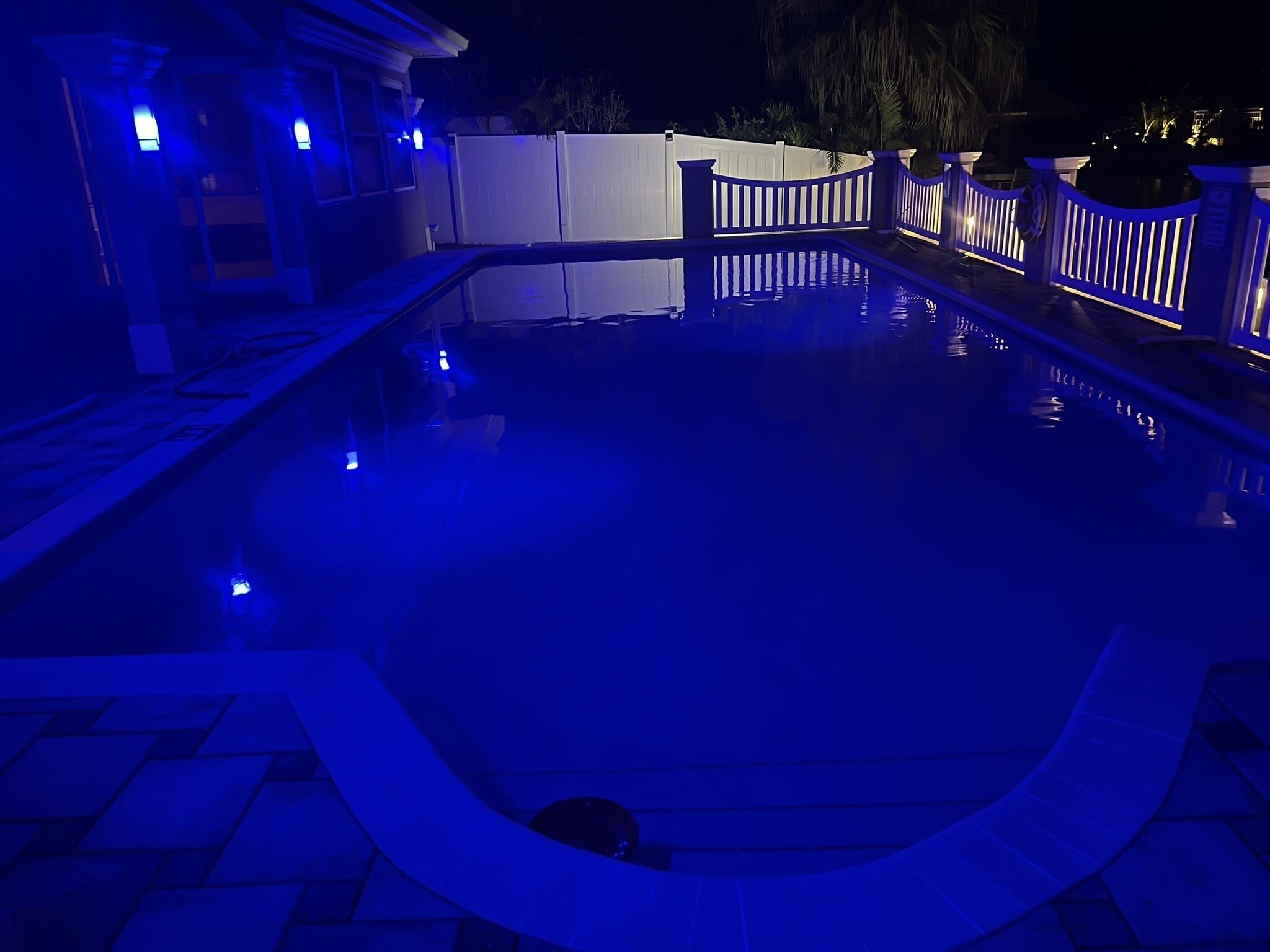 A swimming pool with a wooden deck and a white fence.