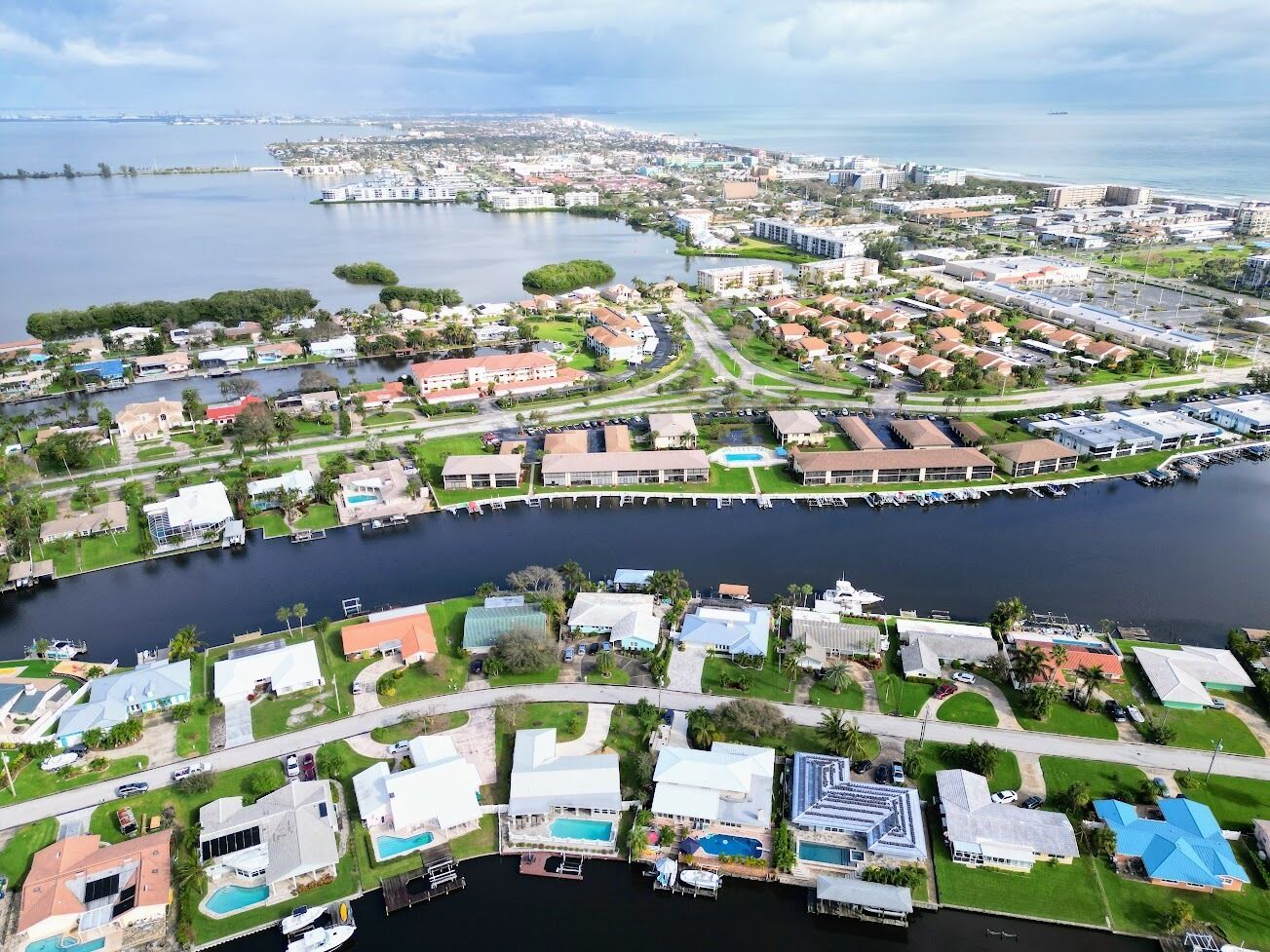 An aerial view of a coastal residential area with houses, a marina, and a large body of water.