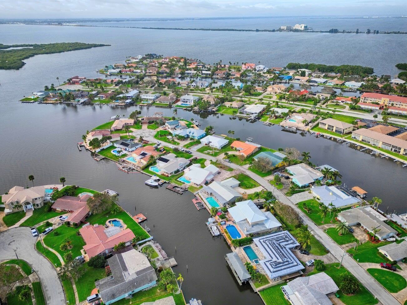 Vue aérienne d’un quartier résidentiel avec des maisons, des piscines et un port de plaisance.