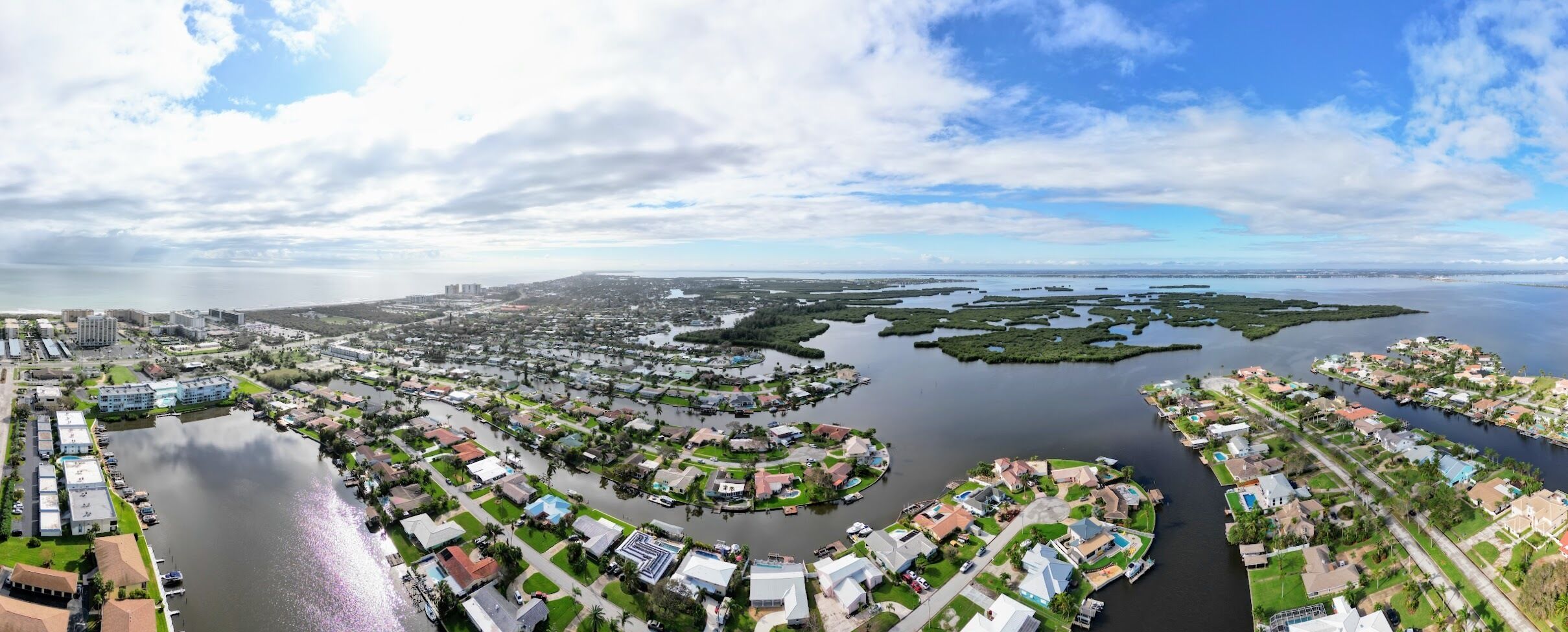 An aerial view of a coastal residential area with houses, a marina, and a large body of water.