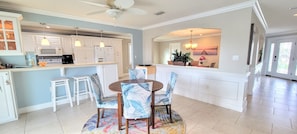 A spacious kitchen with white cabinets, a dining area with a round table and chairs, and a large window with a view of the outdoors. - "Dive Into Fun! Spring & Summer Deals at Dolphin Cove – Walk to It All!" (Cocoa Beach)